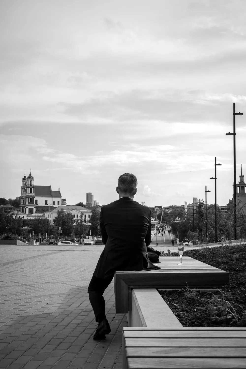 A man sitting on a bench with a champagne glass, looking towards the city view.